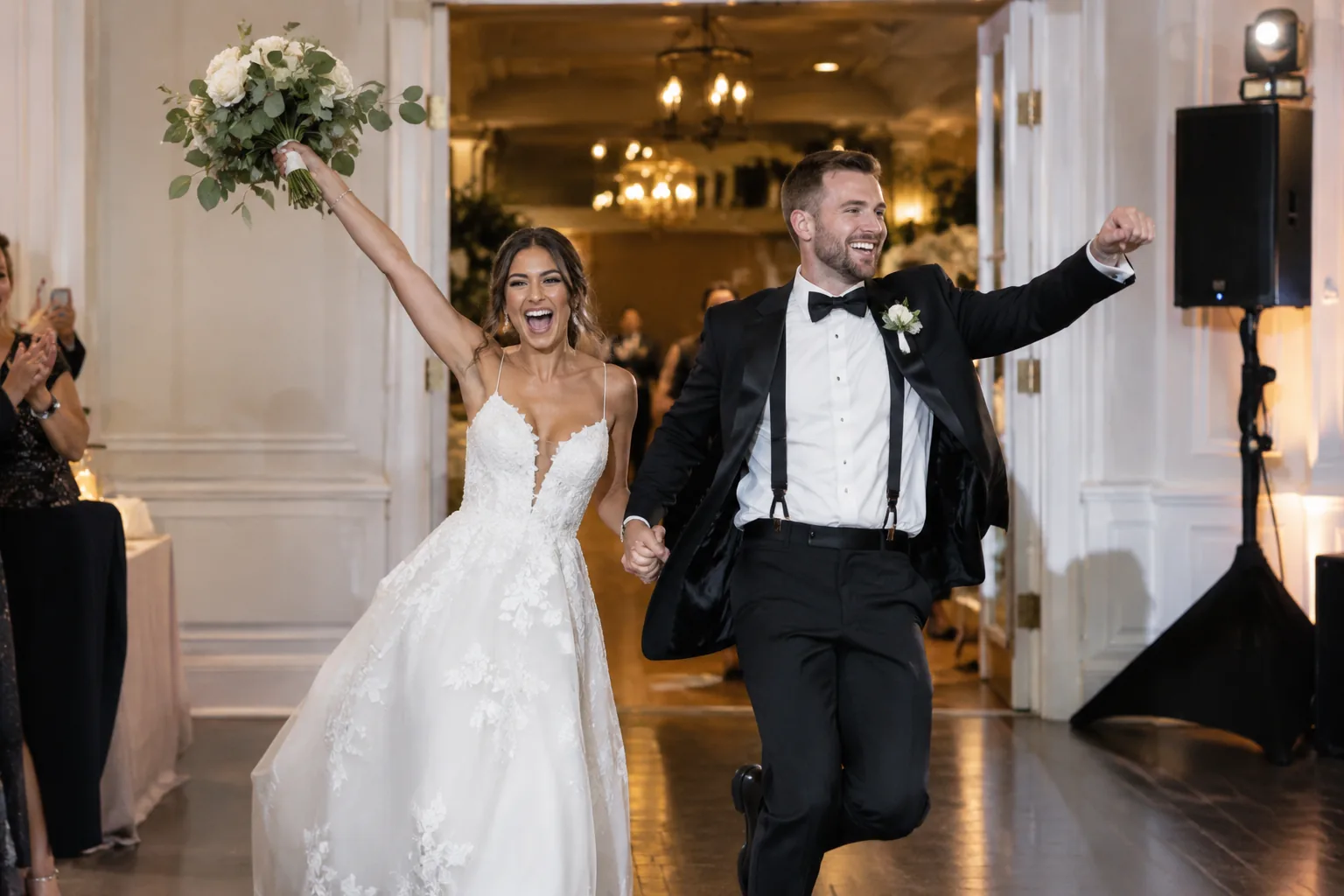 Bride raising her bouquet and groom cheering as they make their grand entrance into the wedding reception