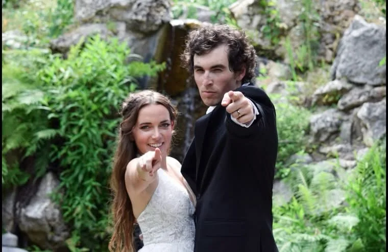 Bride and groom pointing at the camera outside by a waterfall